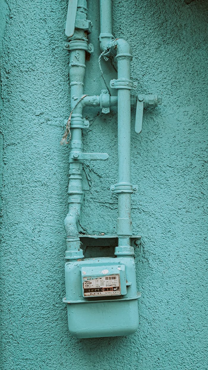 Close-up of a blue gas meter with pipes on a building exterior wall, showcasing industrial design.