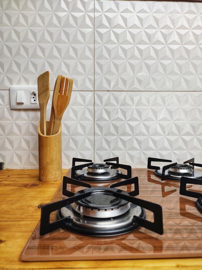 Close-up of a modern kitchen featuring a gas stove and wooden utensils against patterned wall tiles.