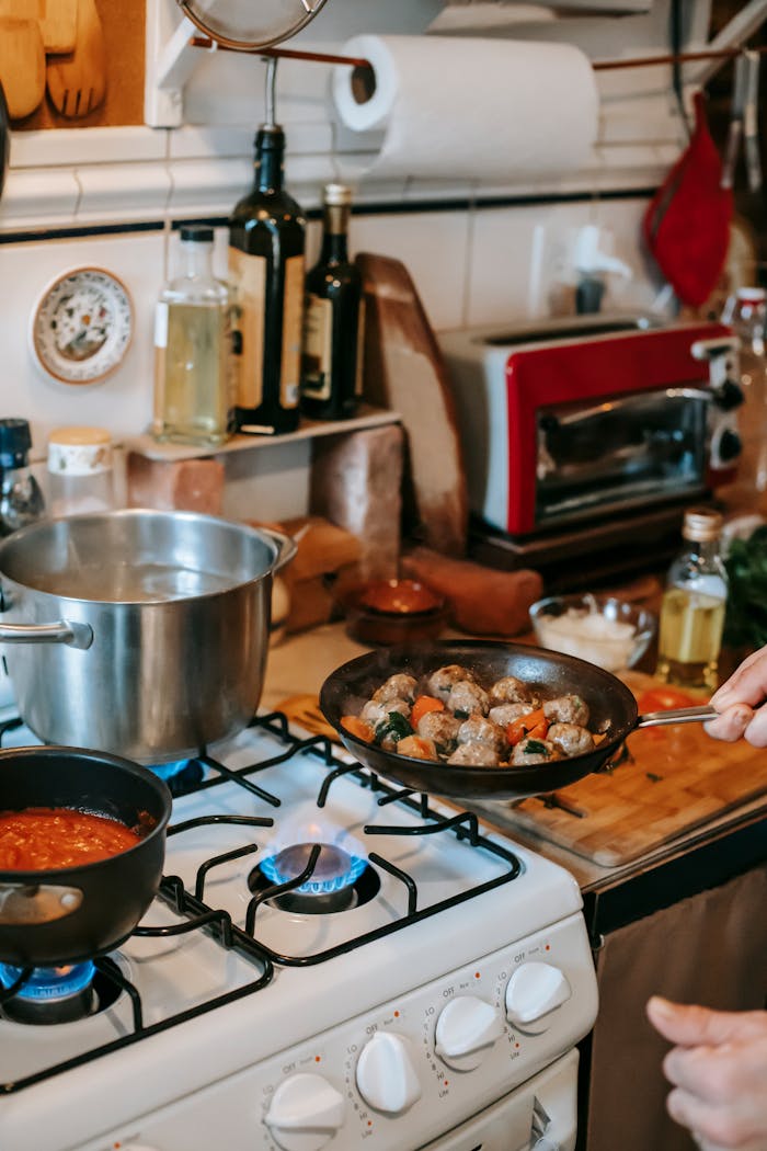 A cozy kitchen setting with meatballs frying on the stove and sauce simmering nearby.